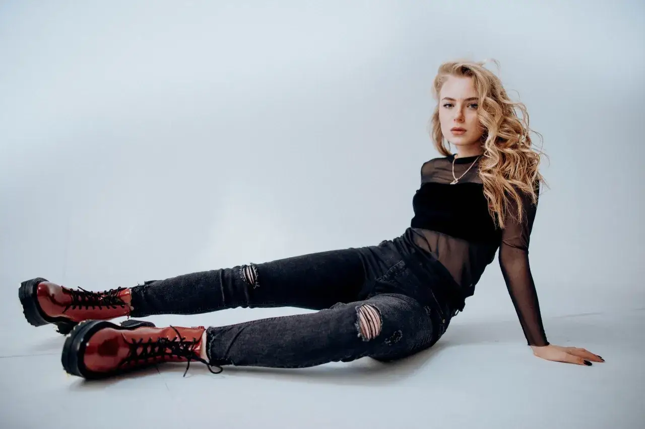Blondynka w czarnym, prześwitującym topie i podartych jeansach, z rudymi botkami na platformie, emanuje rock style.