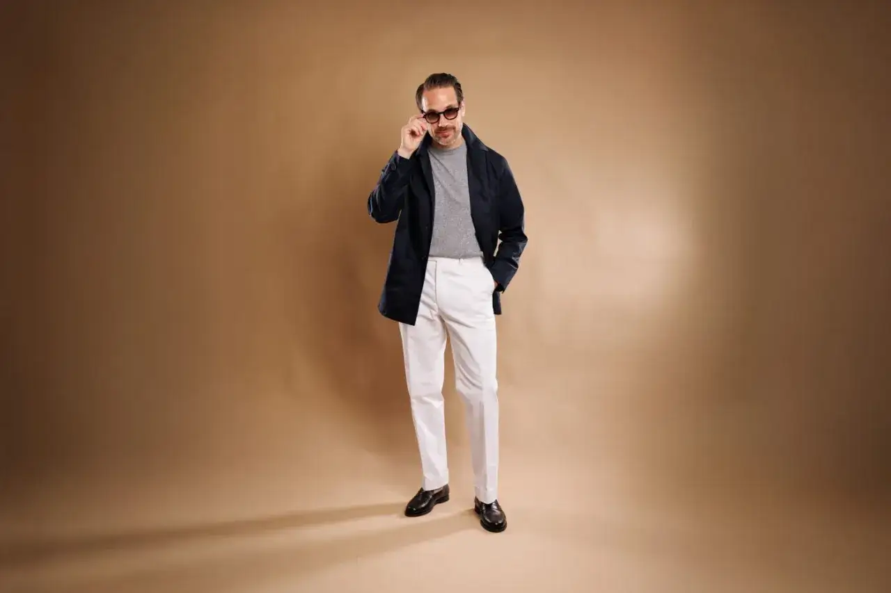 Mężczyzna w granatowej marynarce, szarym golfie i białych spodniach prezentuje styl smart casual.
