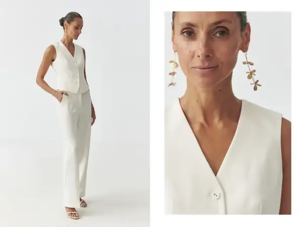 Elegancka kamizelka damska w kremowym kolorze, idealna do stylizacji z szerokimi spodniami. Długie, złote kolczyki dodają szyku.