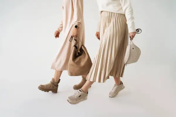 Dwie kobiety prezentują jesienne stylizacje. Jedna w beżowej sukience i botkach, druga w plisowanej spódnicy i sneakersach. Idealne buty na jesień.