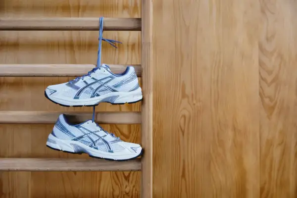 Białe buty sportowe z niebieskimi detalami wiszą na drabince gimnastycznej. Idealne buty na WF, gotowe do treningu.