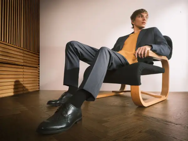 Mężczyzna w granatowej marynarce i musztardowym swetrze, spodnie i eleganckie buty tworzą stylowy ubiór casual.