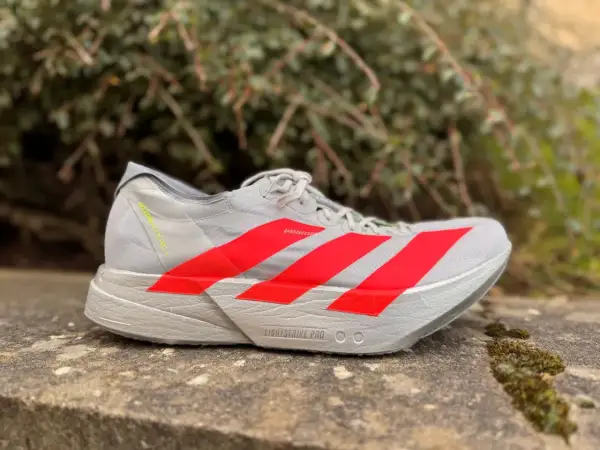 Szary but biegowy adidas adios pro 4 z czerwonymi paskami, gotowy na szybkie trasy.