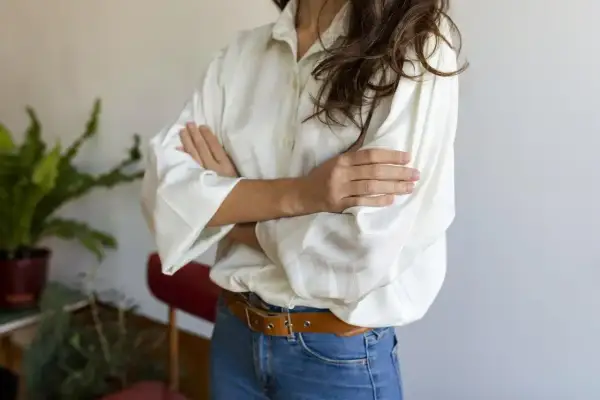 Kobieta w białej koszuli oversize i jeansach, z paskiem. Pokazuje, jak nosić koszulę oversize, tworząc luźny, ale stylowy look.