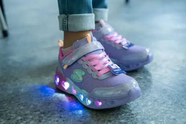 Fioletowe buty dziecięce z brokatem i różowymi sznurówkami. Ich podeszwa świeci kolorowymi serduszkami, tworząc magiczny efekt.