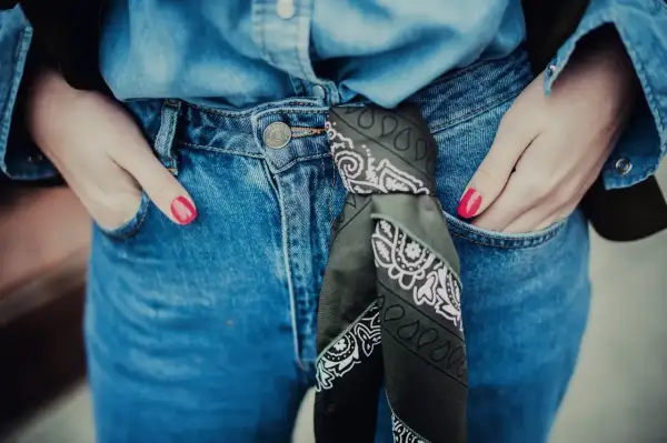 Dżinsy i koszula w stylu denim, z bandaną zawiązaną w pasie. Ręce w kieszeniach, paznokcie pomalowane na jaskrawy róż. Jak zawiązać bandanę? Oto inspiracja.