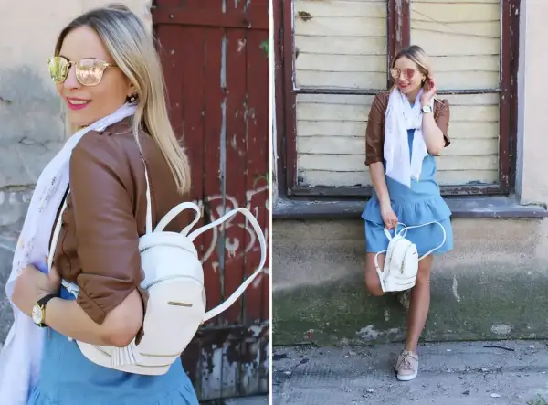 Kobieca stylizacja: jeansowa sukienka, brązowa ramoneska, biały plecaczek i beżowe sneakersy. Idealne buty do jeansowej sukienki na co dzień.